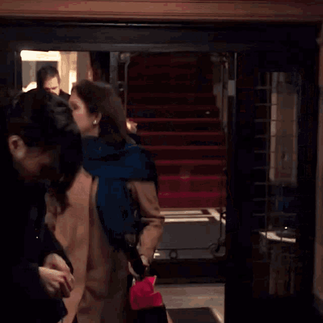 a woman in a blue scarf is standing in front of a red carpeted staircase