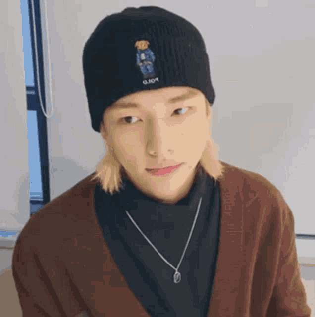 a young man wearing a black beanie and a brown cardigan is looking at the camera .