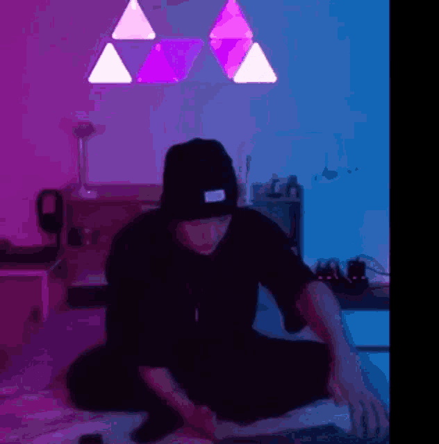 a man in a black hat is sitting on the floor in a room with purple and blue lights .