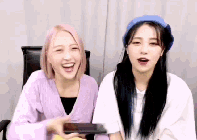 two girls are sitting next to each other and laughing while looking at a tablet .