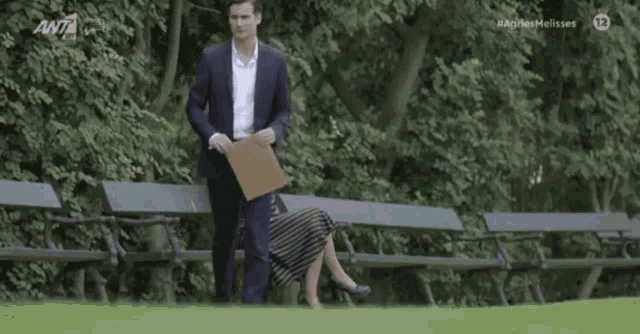 a man in a suit stands next to a woman sitting on a park bench with the number 12 on the bottom left