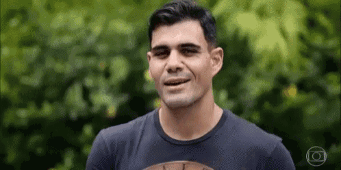 a man in a black shirt is smiling and looking at the camera while standing in front of trees .