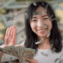 a woman is holding a bunch of money and smiling while money is falling on her face .