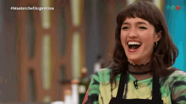 a woman in an apron is laughing in front of a screen that says masterchef argentina
