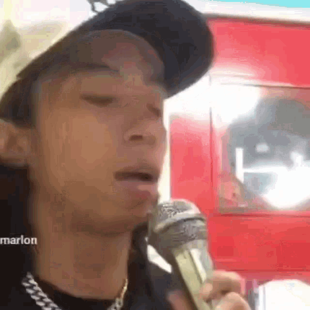 a man is singing into a microphone while wearing a hat and chain .