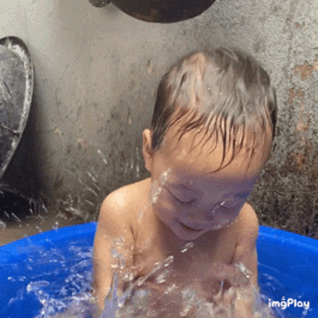 a baby is taking a bath in a blue bucket with the words imgplay visible on the bottom