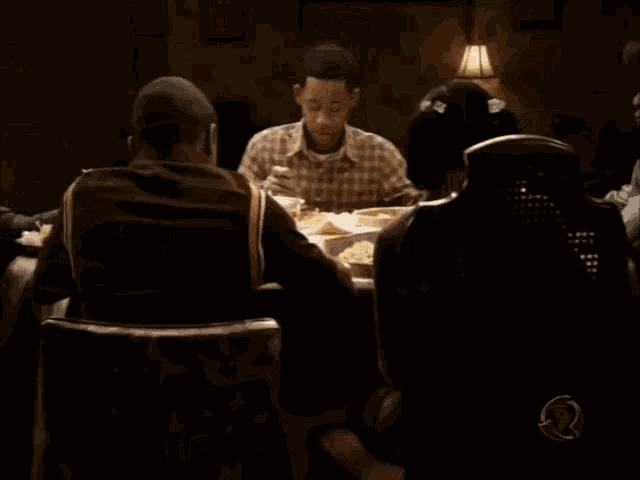 a man in a plaid shirt sits at a table with other people eating food