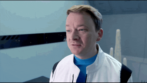 a man wearing a white jacket and a blue shirt is looking at the camera