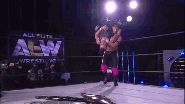 a wrestler is being lifted in the air by another wrestler in front of an all elite wrestling sign