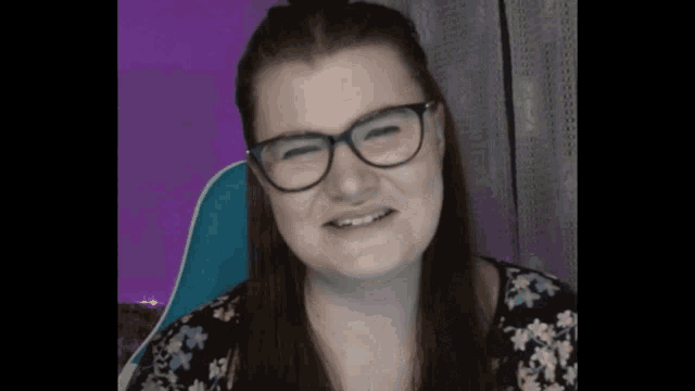 a woman wearing glasses and a floral shirt is smiling and looking at the camera .