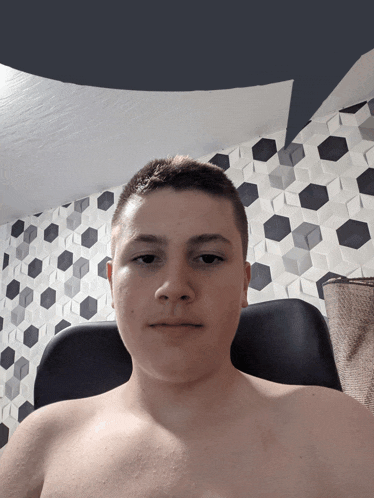 a shirtless young man is sitting in front of a wall with soccer balls on it
