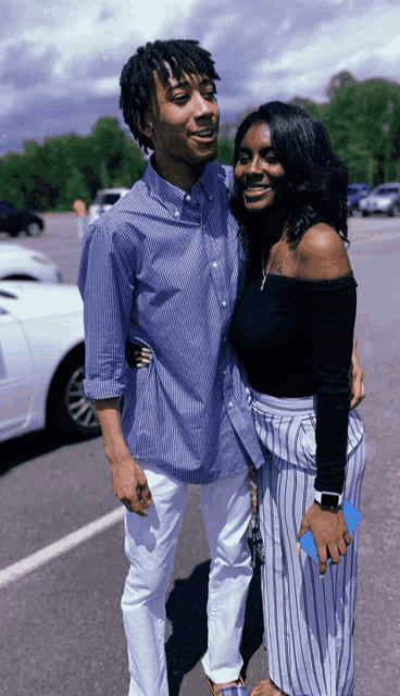 a man and a woman are posing for a photo in a parking lot