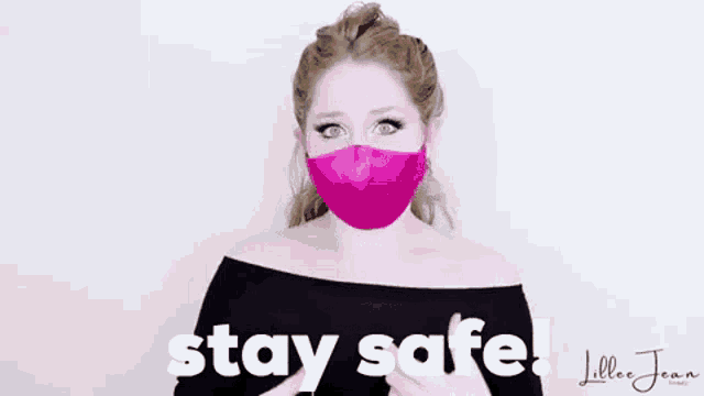 a woman wearing a pink face mask is holding her hand up and saying `` stay safe '' .