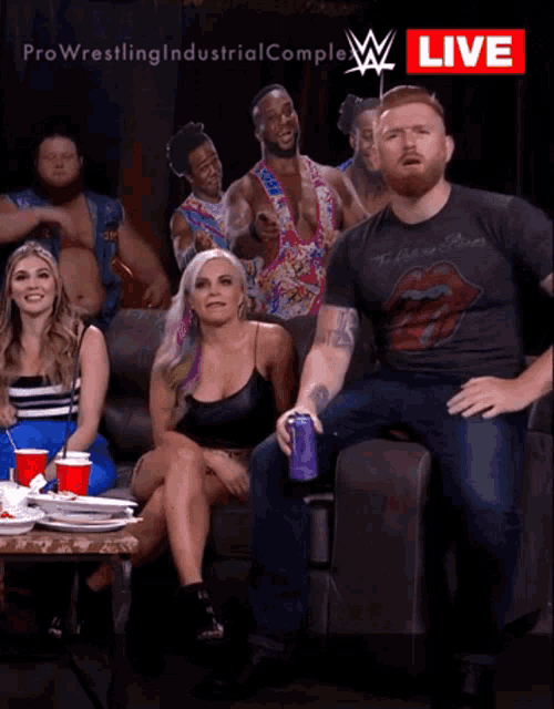 a group of wrestlers are sitting on a couch in front of a pro wrestling industrial complex live sign