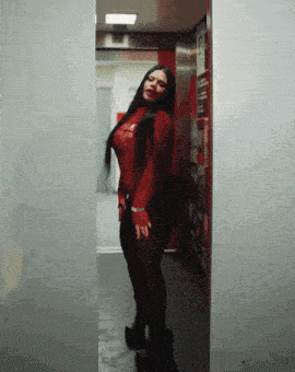 a woman in a red top and black pants is standing in an elevator