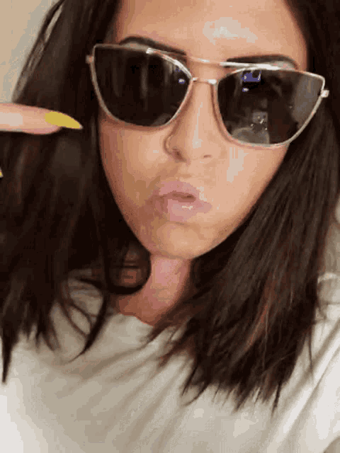a woman wearing sunglasses and a white shirt makes a face