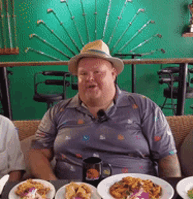a man wearing a hat sits at a table with plates of food in front of him