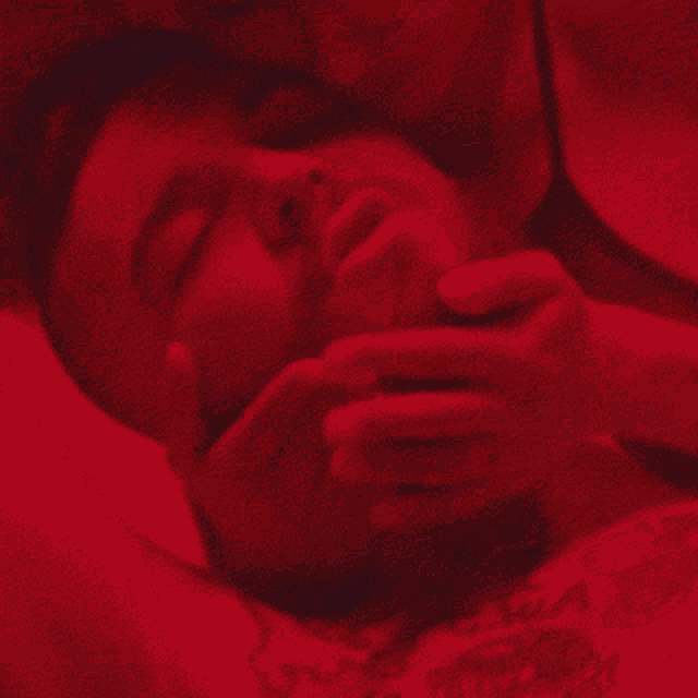 a man laying on a bed with a woman holding his face in red light