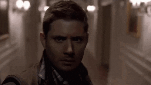 a man in a trench coat is standing in a dark hallway looking at the camera .