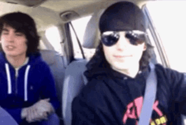 a man wearing sunglasses and a bandana is driving a car with another man sitting in the back seat .