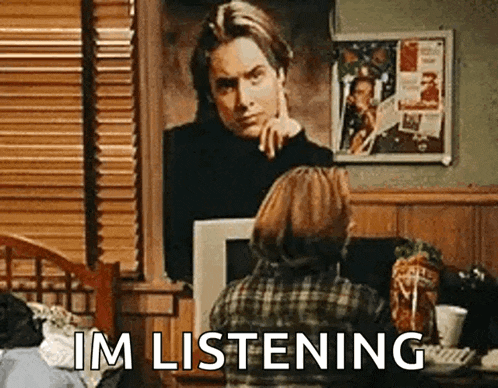 a woman is sitting at a table in front of a painting of a man and says `` im listening '' .