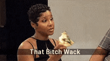 a woman is holding a piece of food in her hand and says that bitch wack .