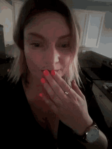 a woman with red nails and a watch on her wrist covers her mouth