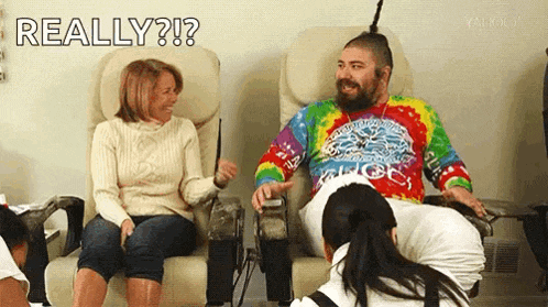 a man in a tie dye shirt is sitting next to a woman in a chair and laughing .