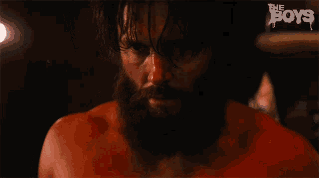 a shirtless man with a beard is in a dark room with the words the boys behind him