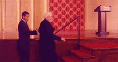 two men are shaking hands on a stage in front of a podium with the letter i on it .