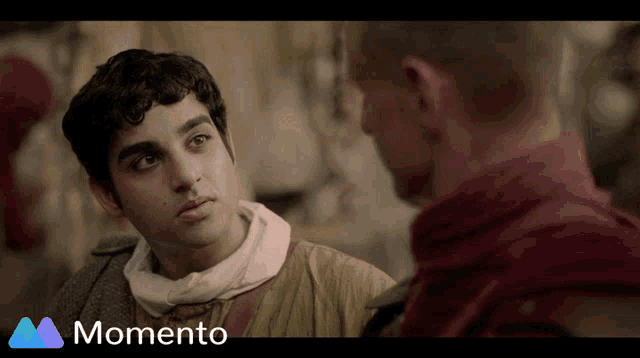 a man in a red robe talks to another man in a momento video