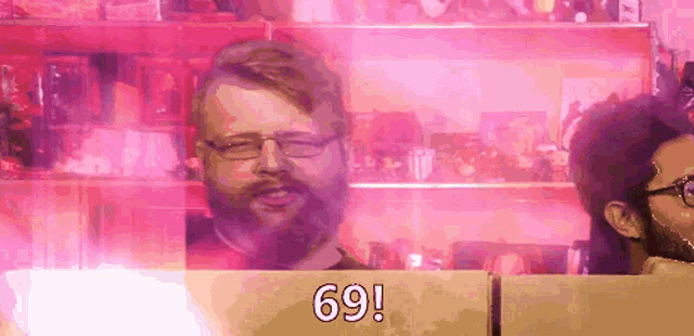 a man with glasses and a beard stands in front of a pink wall with the number 69 on it