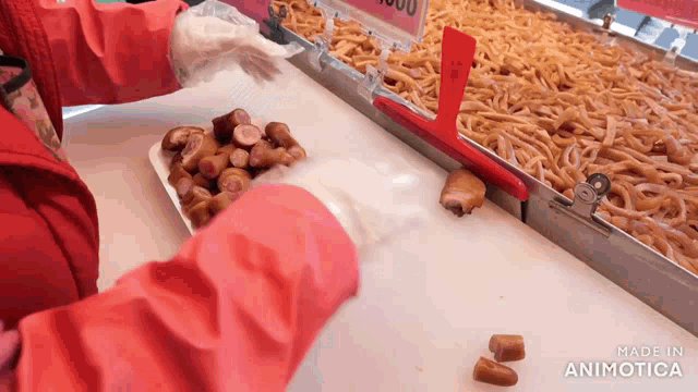 a person in a red jacket is putting a tray of food on a conveyor belt that says made in animotica