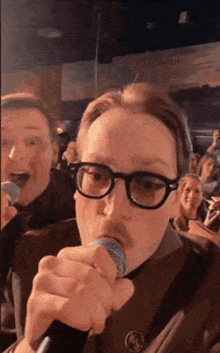 a man wearing glasses and a mustache sings into a microphone