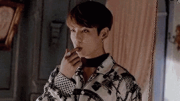a young man is smoking a cigarette in a room while wearing a choker around his neck .