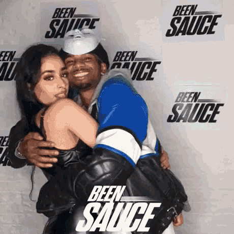 a man is hugging a woman in front of a wall with been sauce signs