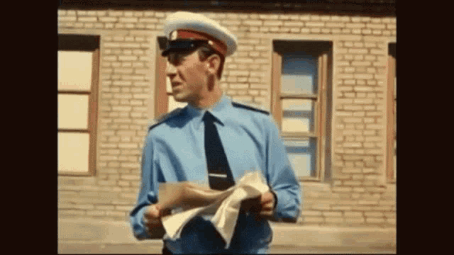 a man in a blue shirt and tie is holding papers in front of a brick building