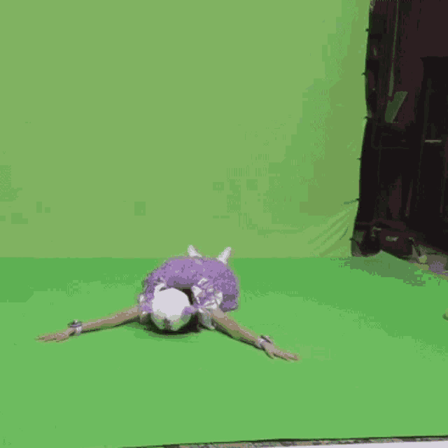 a woman in a purple dress is laying on the floor with her arms outstretched in front of a green screen .
