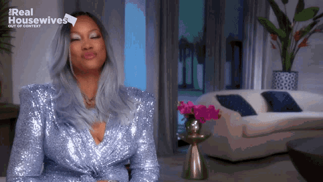 a woman wearing a blue sequined dress is sitting in a living room with a sign that says real housewives