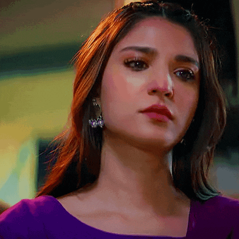 a close up of a woman 's face wearing earrings and a purple top