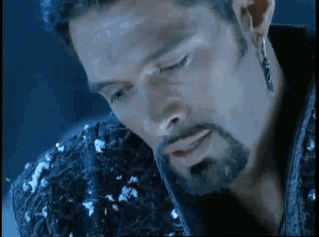 a close up of a man with a beard wearing earrings and a sequined jacket .