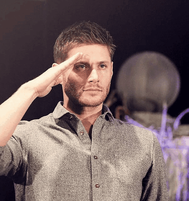 a man in a grey shirt salutes with his hand