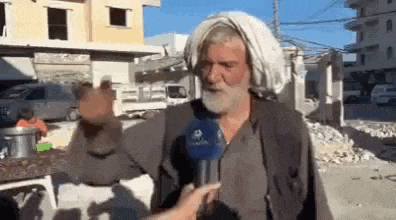 a man with a beard is talking into a microphone while wearing a white turban .