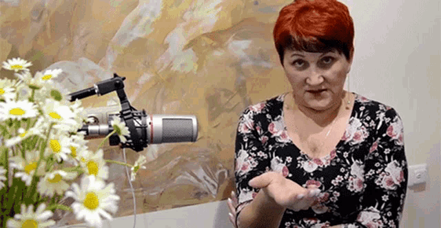 a woman with red hair is standing in front of a microphone with flowers in the background .