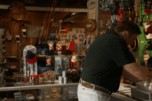 a man working in a store with a sign on the wall that says ' fishing tackle shop '
