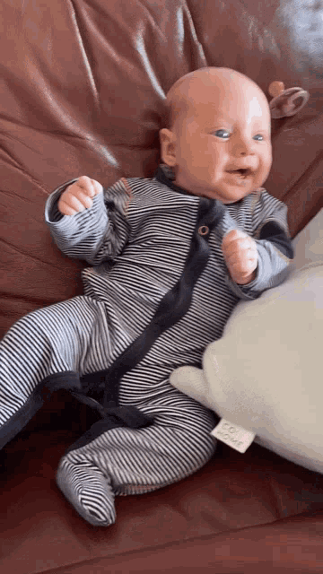 a baby in a striped outfit is laying on a couch next to a pillow that says first