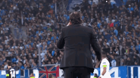 a man in a black suit is standing on a soccer field holding his head .
