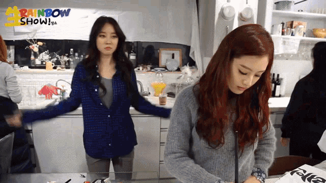 two women are standing in a kitchen with the words rainbow show on the wall behind them