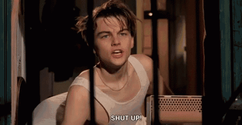 a young man in a white tank top is sitting in a room and talking to someone .
