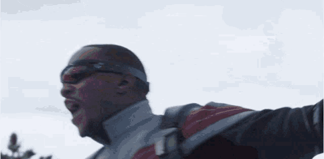 a man wearing sunglasses and a backpack is screaming with his arms outstretched .